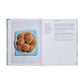 An open copy of Phaidon's "The Spanish Mediterranean Islands Cookbook" shows a photo of round buns on the left page and the "Anytime Buns" recipe with Mediterranean instructions and ingredients on the right.