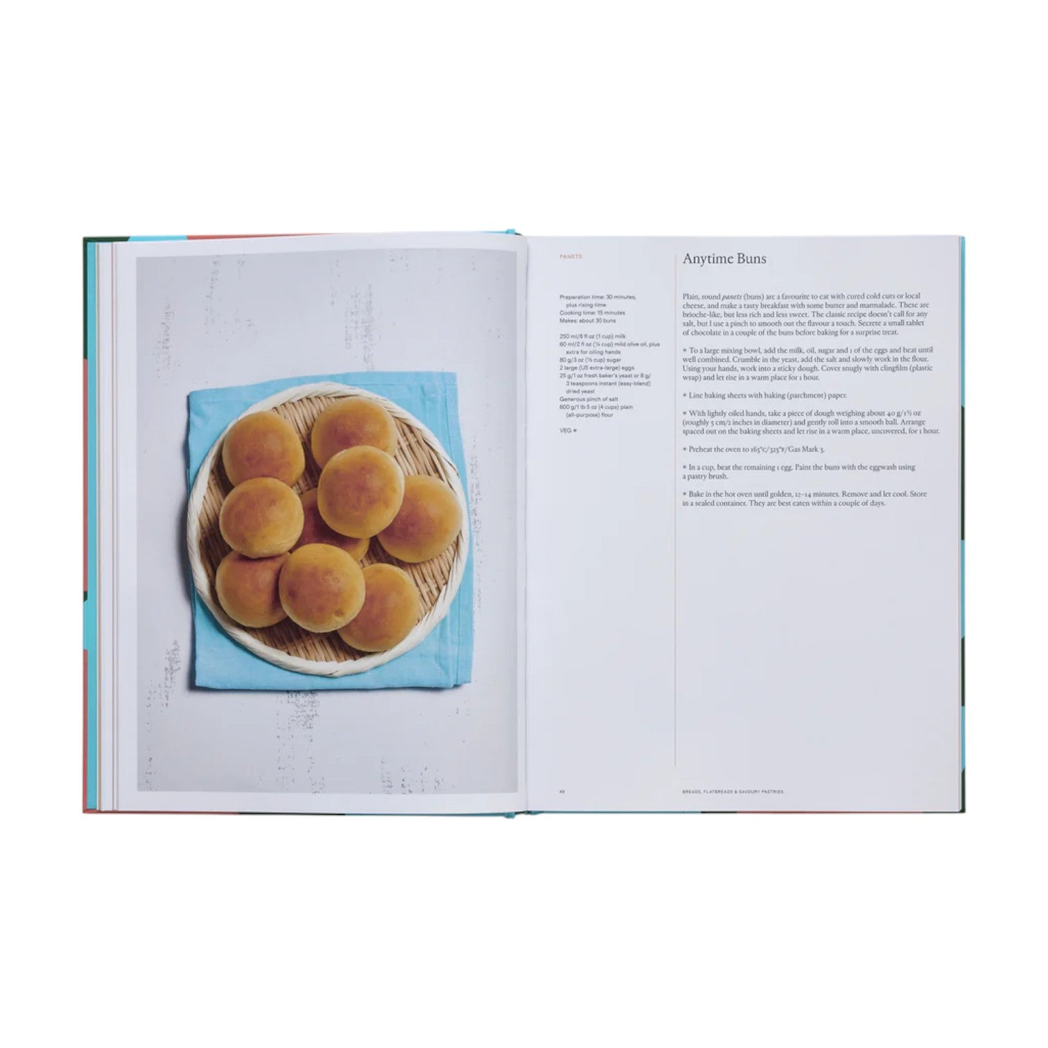 An open copy of Phaidon's "The Spanish Mediterranean Islands Cookbook" shows a photo of round buns on the left page and the "Anytime Buns" recipe with Mediterranean instructions and ingredients on the right.