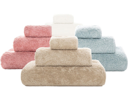The Graccioza Egoist Bath Collection features four sets of high-density, fluffy towels in beige, pink, white, and blue, stacked in three sizes and neatly arranged side by side on a white background.