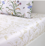 A bed made with Botanic Bedding Collection organic cotton sateen sheets featuring a monochromatic botanical print, paired with a pillowcase decorated with colorful floral and insect illustrations.