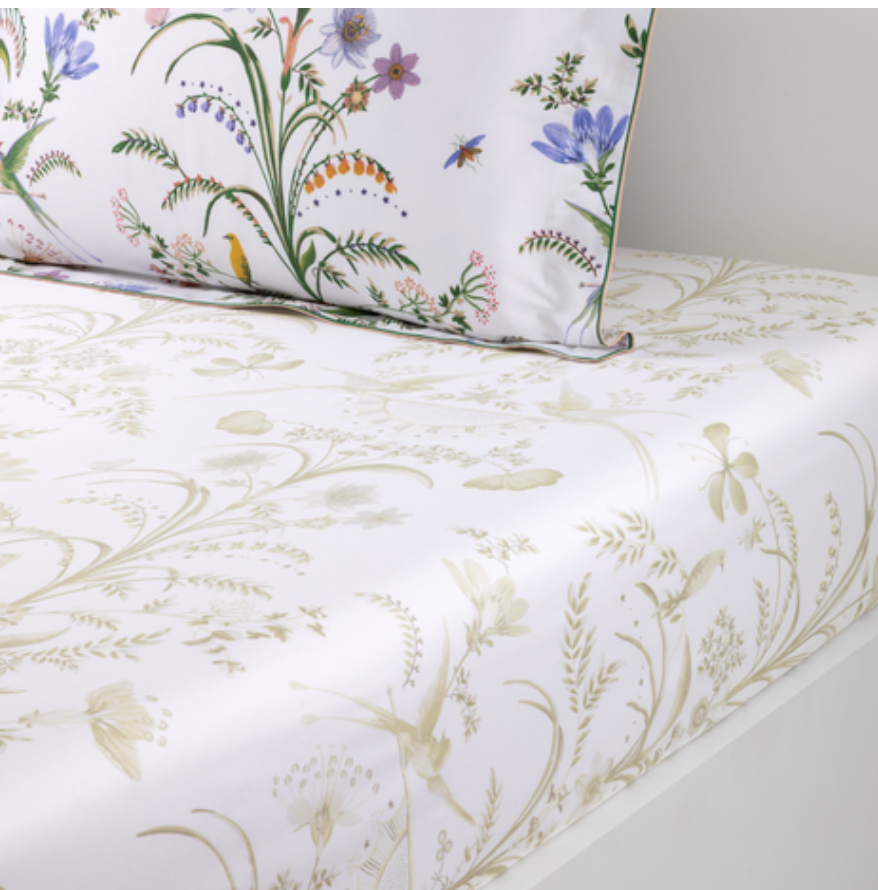 A bed made with Botanic Bedding Collection organic cotton sateen sheets featuring a monochromatic botanical print, paired with a pillowcase decorated with colorful floral and insect illustrations.