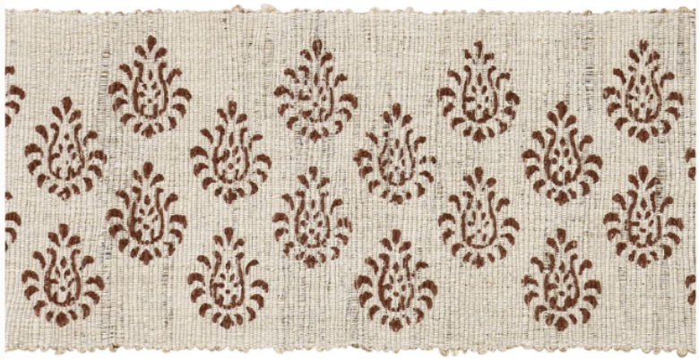 A rectangular woven beige rug with brown floral motifs arranged in rows pairs beautifully with the Bunny Williams Grant Sofa, enhancing any living space—modern or traditional.