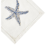 A white cloth napkin from Haute Home’s Starfish Coaster & Bath Collection, crafted from Italian linen, showcases a blue and white embroidered starfish in one corner and decorative stitching along the edges—an elegant accent that pairs beautifully with other luxurious linen coasters and refined home décor pieces.