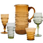 The Ella Drinkware Collection by Juliska features five vintage-inspired glasses and a pitcher, all mouth-blown with ribbed spiral designs in amber and light green.