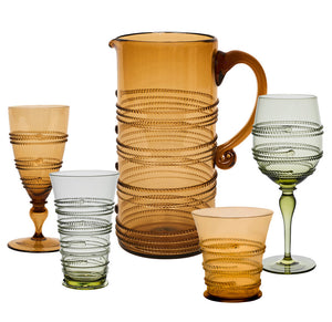 The Ella Drinkware Collection by Juliska features five vintage-inspired glasses and a pitcher, all mouth-blown with ribbed spiral designs in amber and light green.