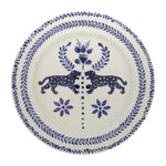 The Casa Deep Navy Dinnerware Collection by Johanna Ortiz features white ceramic plates with blue motifs—two mirrored spotted animals facing a central floral design—showcasing hand-painted artistry and the heritage of Carmen de Viboral clay.