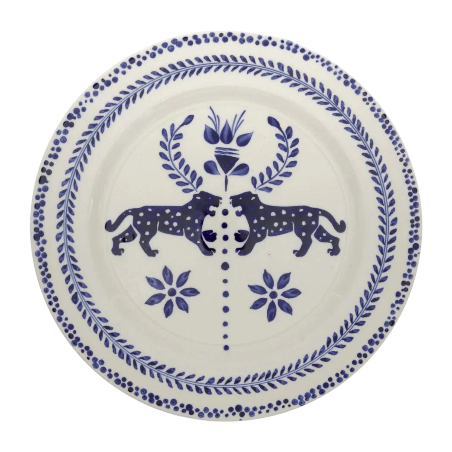 The Casa Deep Navy Dinnerware Collection by Johanna Ortiz features white ceramic plates with blue motifs—two mirrored spotted animals facing a central floral design—showcasing hand-painted artistry and the heritage of Carmen de Viboral clay.