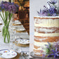 A neatly set dining table with floral plates and tall purple flowers, inspired by entertaining ideas from “An Entertaining Story” by Common Ground; beside it, a naked layered cake topped with purple blooms serves as picture-perfect party inspiration.
