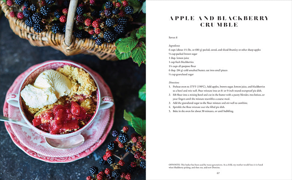 A bowl of apple and blackberry crumble with vanilla ice cream sits on a floral plate, providing perfect party inspiration from Common Ground’s “An Entertaining Story” by India Hicks; a basket of blackberries and recipe text are also visible.