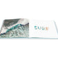 Open Escape travel photography book by Gray Malin displaying an aerial view of ocean waves on the left page and the word “SURF” on the right.