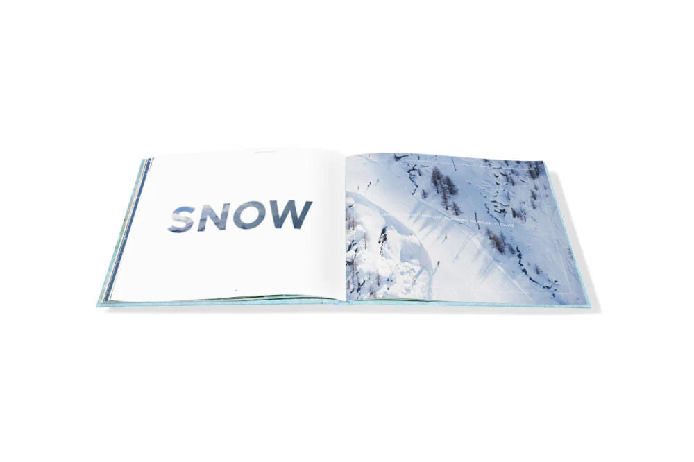 An open Escape travel photography book displays the word “SNOW” on the left page and an aerial photograph of a snowy mountain slope on the right.