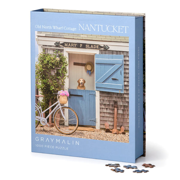 Enjoy the 1000-piece Gray Malin Nantucket Puzzle by Chronicle Books, showcasing a quaint cottage with a dog at the half-door and a blue bike with pink flowers, evoking idyllic coastal charm.