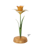 The Meadow Walk Daffodil Candle Holder Collection by Juliska features a 9-inch tall decorative flower sculpture with a green stem and leaves, yellow and orange petals, and a gold circular base.