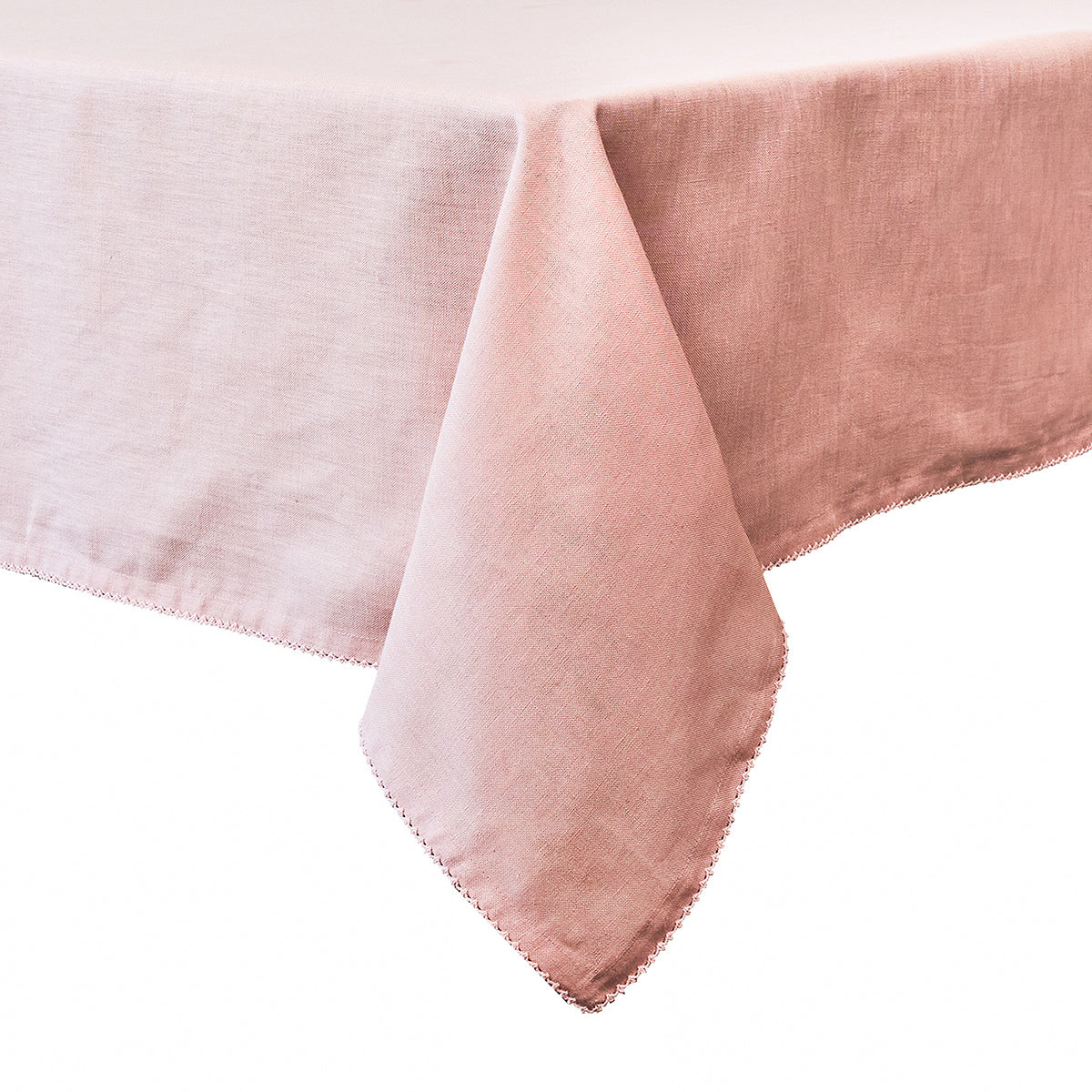 The Juliska Pink Berry Scallop Tablecloth in light pink linen, featuring a scalloped trim, is draped over the corner of a rectangular table against a white background.