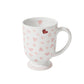 This white ceramic mug from Juliska’s Love You More Decor and Tabletop Collection features pink and red hearts with a pedestal base—ideal to match with pink heart plates or other sweet tableware for a charming, love-themed setting.