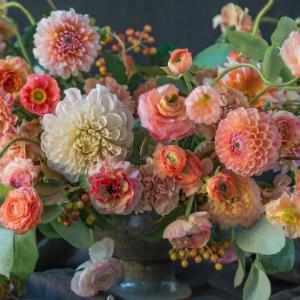 A stunning floral arrangement featuring pink, peach, and cream blooms accented with green foliage in a dark vase set against a dramatic background, inspired by Kiana Underwood’s signature style as showcased in Chronicle Books’ “Color Me Floral.”.