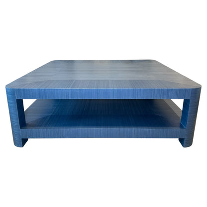 The Series O Custom Cocktail Table by T3 Custom Furniture is a square blue table with rounded edges, a lower shelf, and a textured azure finish inspired by Manila hemp.