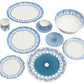 The Pink House Mustique Azure Blue Dinnerware Collection features custom ceramic plates, bowls, and mugs with blue geometric and floral patterns, beautifully arranged on a white background.