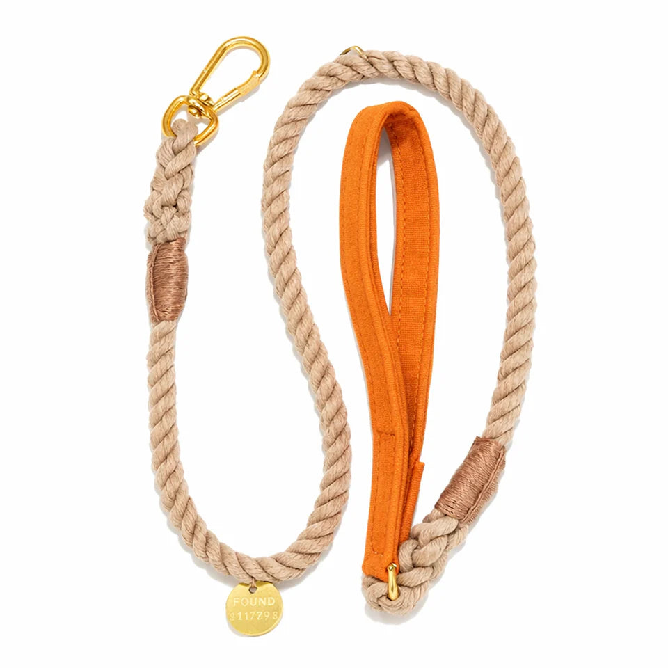 The Found My Animal Waxed Cotton Canvas Leash Collection features a handcrafted rope dog leash with gold hardware, an orange waxed canvas handle, and a round gold tag engraved with "FOUND 11796.