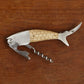 The Finest Catch 3 in 1 Bottle Opener by Two's Company features a fish-shaped design with corkscrew, foil cutter, and wine knife—ideal as a unique fishing gift and shown here resting on a wooden surface.