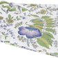 The Matouk Pomegranate Roman Linen Bedding Collection in Lilac features a folded white linen fabric with a floral pattern of green leaves and purple, blue, and yellow flowers.