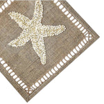 The Haute Home Starfish Coaster Set features beige burlap coasters with embroidered starfish made of small white seashells, bringing a stylish coastal touch to your table.