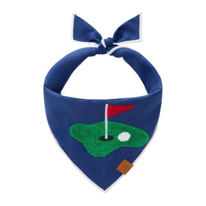 The Foggy Dog Golf Applique Dog Bandana features a golf green, hole, red flag, and ball embroidery with a knot top and brown tag—making it a unique golf accessory and perfect caddie gift.