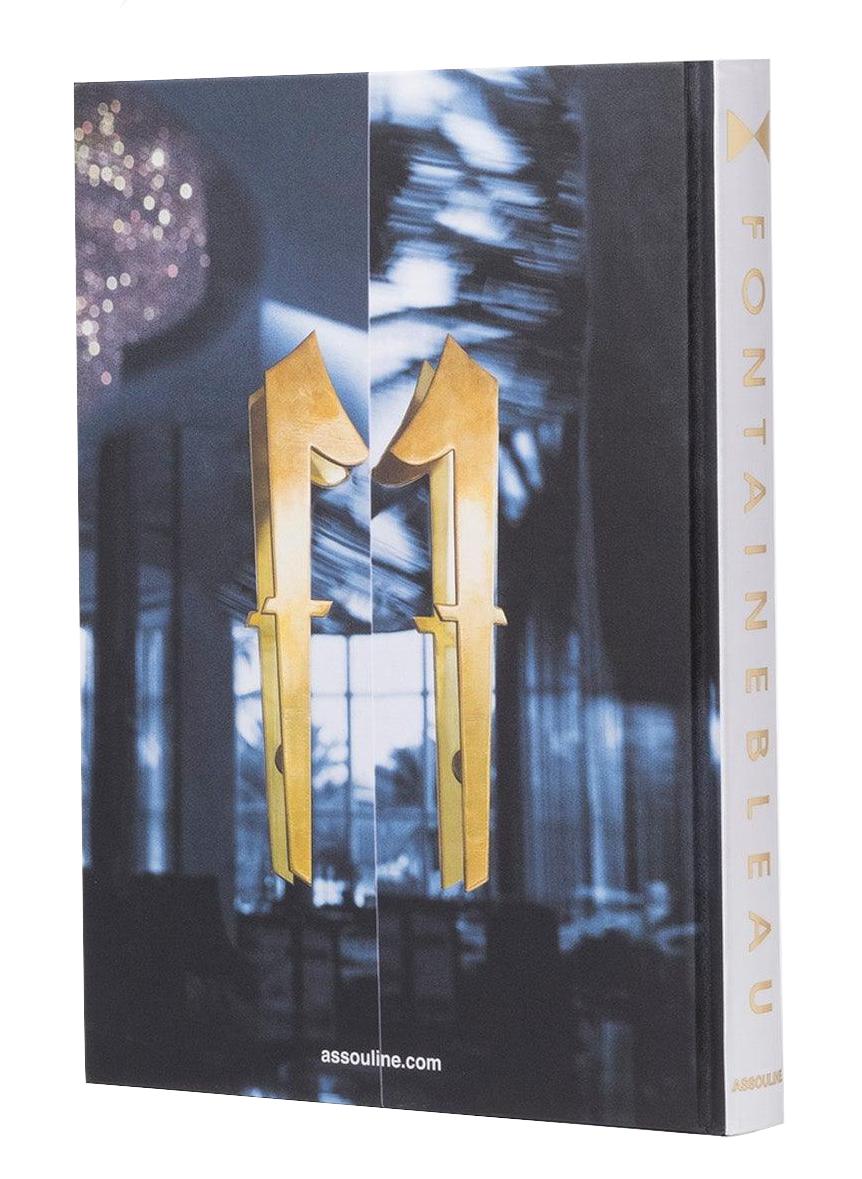 The Assouline book "Fontainebleau" features a gold geometric cover design inspired by architectural marvels. The title is displayed vertically on the spine, echoing its luxurious namesake hotel, and includes the publisher's website elegantly at the bottom.