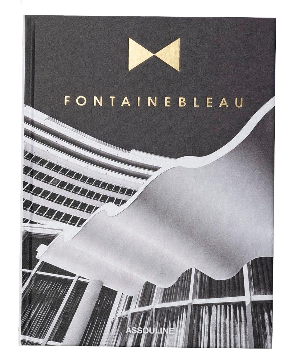 The Assouline book "Fontainebleau" features a black-and-white cover image of architectural beauty, adorned with gold lettering. It exudes luxury, reflecting the grandeur reminiscent of the iconic Fontainebleau hotel.