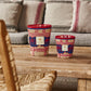 Two colorful woven baskets on a wooden coffee table in a cozy living room with a gray sofa, a wicker chair, and Baobab Collection Frida Draozy Frida candles.