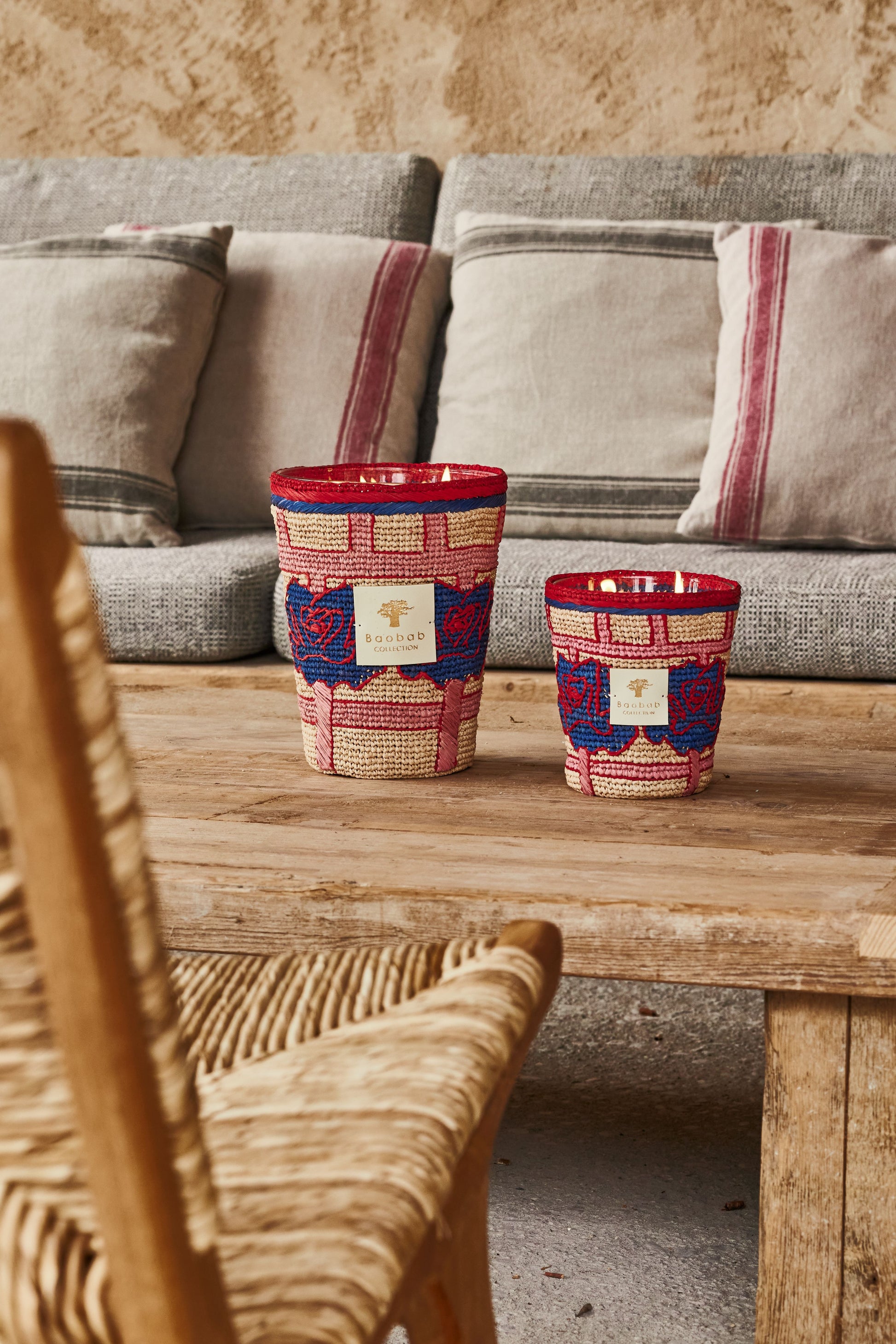 Two colorful woven baskets on a wooden coffee table in a cozy living room with a gray sofa, a wicker chair, and Baobab Collection Frida Draozy Frida candles.