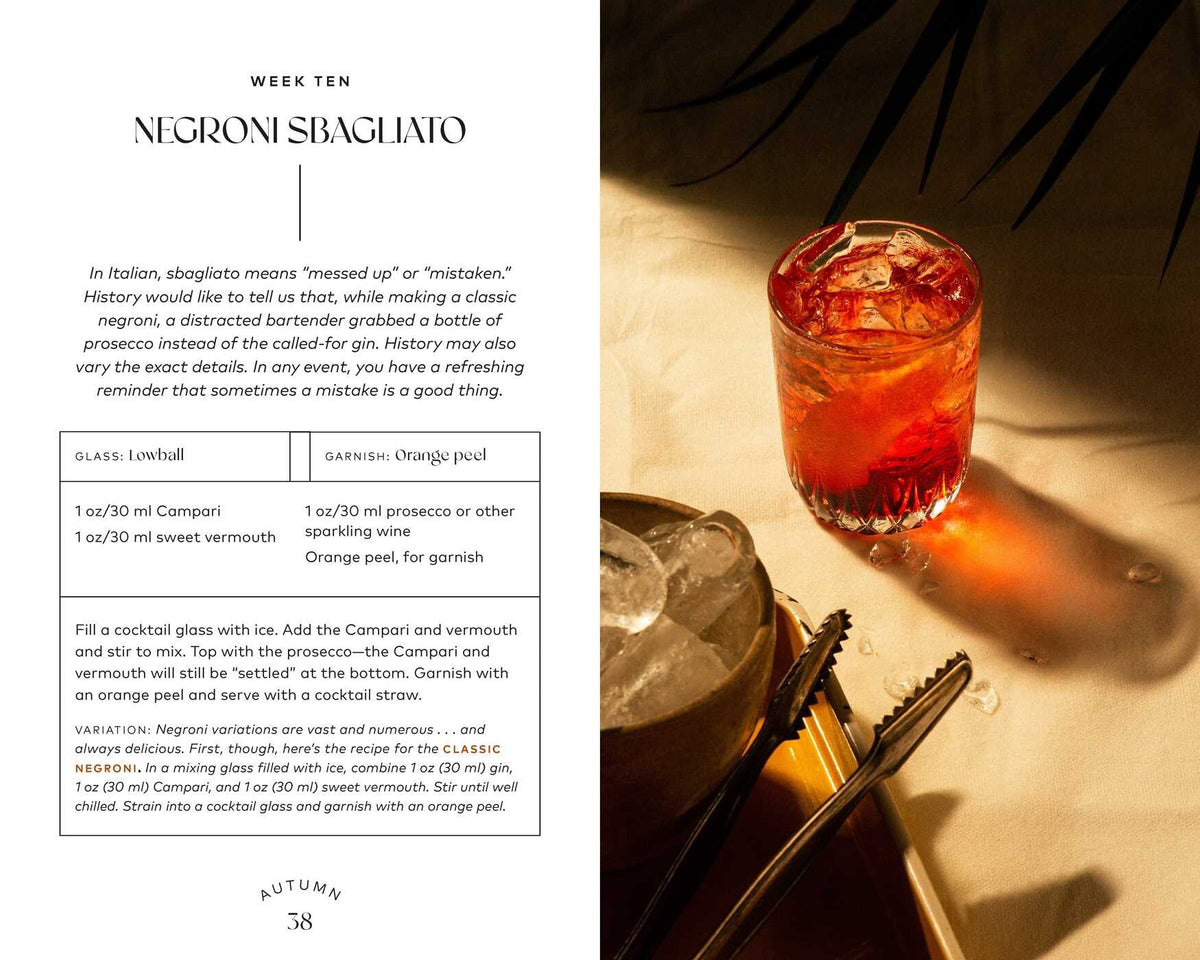 A glass of Negroni Sbagliato—served over ice with a twist of orange peel—rests on a sunlit table beside a white napkin and metal tongs, making it an ideal recipe from Simon & Schuster’s Friday Night Cocktails for anyone seeking delicious homemade mixed drinks.