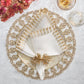 A white napkin with gold trim, folded decoratively and held by the Kim Seybert Fringe Napkin Ring, rests on a gold geometric charger beside a glass and pink flowers for a glamorous look.