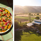 A vibrant citrus salad, inspired by California cuisine and seasonal recipes from Full Belly by Chronicle Books, rests on a tiled table beside an overhead view of an outdoor gathering at an organic family farm, with sprawling fields and distant mountains creating a stunning backdrop.