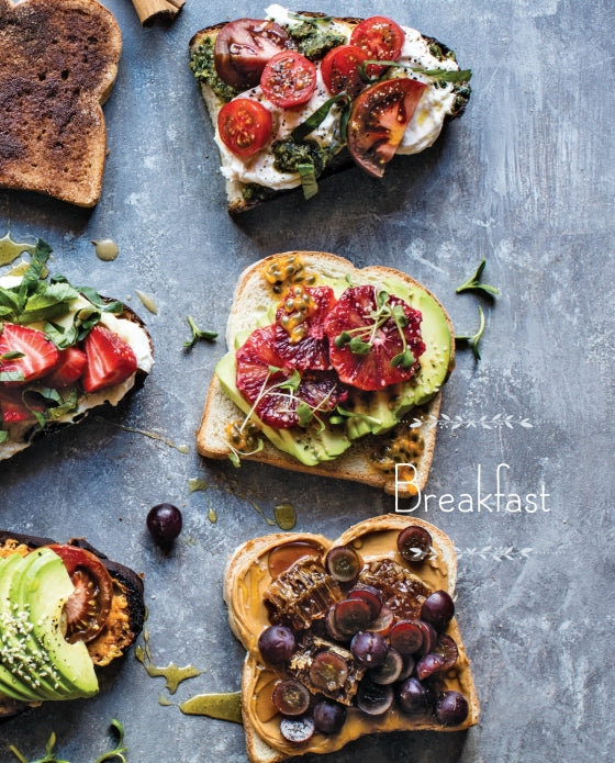 Four slices of toast topped with an array of fruits, vegetables, and spreads are artfully arranged on a gray surface beside the word “Breakfast”—a cozy and inviting scene inspired by recipes from the Half Baked Harvest Cookbook by Penguin Random House.
