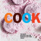 Three round, pink, powdered treats rest on a white surface next to a copy of “Cookies” by Penguin Random House—an inspiring collection for dessert lovers and anyone browsing recipes for anytime treats.