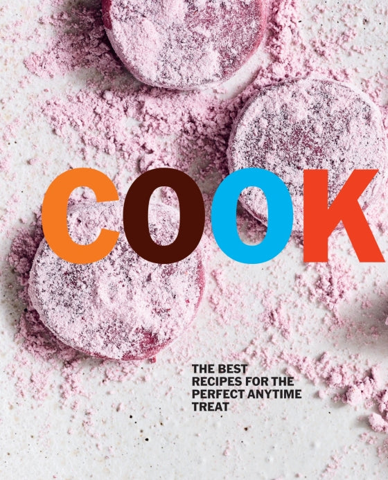 Three round, pink, powdered treats rest on a white surface next to a copy of “Cookies” by Penguin Random House—an inspiring collection for dessert lovers and anyone browsing recipes for anytime treats.