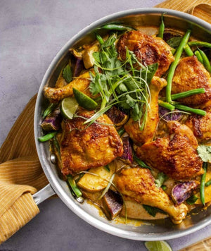 Enjoy a delicious pan of cooked chicken legs with green beans, purple onions, lime wedges, and fresh cilantro garnish—all featured in Dinner Tonight by Penguin Random House. Perfect for easy cleanup and ideal for stress-free weeknight dinners.