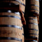 Barrels of Kentucky bourbon, stacked and bound by metal bands in a dimly lit aging room, evoke the timeless tradition celebrated in Bourbon, The Story of Kentucky Whiskey by Penguin Random House—a vivid tribute to the enduring heritage of America’s historic spirit.