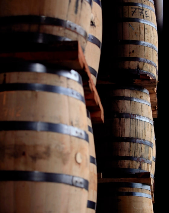Barrels of Kentucky bourbon, stacked and bound by metal bands in a dimly lit aging room, evoke the timeless tradition celebrated in Bourbon, The Story of Kentucky Whiskey by Penguin Random House—a vivid tribute to the enduring heritage of America’s historic spirit.