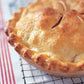 A golden-brown baked pie with a flaky crust, inspired by recipes from the “Barefoot Contessa Family Style” cookbook by Penguin Random House, cools on a wire rack over a white cloth with red stripes—an ideal treat for everyday cooking and family gatherings.