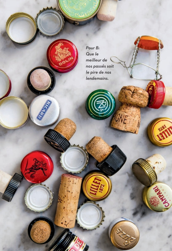 Assorted bottle caps and corks are scattered on a marble surface beside French text reading, “Pour B: Que le meilleur de nos passés soit le pire de nos lendemains,” capturing the spirit of a French apéritif experience as celebrated in Penguin Random House’s Apéritif.