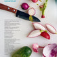 A knife, sliced radishes, a cucumber, and a piece of red onion on a white surface evoke the fresh simplicity of Penguin Random House’s “Kid in the Kitchen” cookbook, with text in the upper left and lower left corners.
