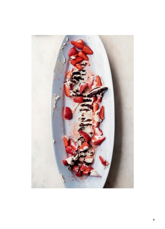 An oval white plate bearing remnants of dessert—scattered strawberry slices, chocolate drizzle, and bits of cream—rests on a light surface, evoking the inviting spirit found in every page of Ottolenghi Comfort by Penguin Random House and celebrating the art of comfort cooking in delectable detail.