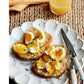 Two slices of toast topped with sliced soft-boiled eggs and herbs grace a white plate, accompanied by a knife, fork, and a glass of orange juice—an inviting scene inspired by recipes from Modern Comfort Food by Ina Garten, published by Penguin Random House, bringing warmth and simplicity to your breakfast table.