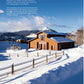 A wooden house nestled in a snowy landscape with a wooden fence out front, majestic mountains behind, and a clear blue sky overhead—an inviting scene reminiscent of the cozy settings found in the Half Baked Harvest Cookbook from Penguin Random House, where comforting recipes bring warmth to every meal.