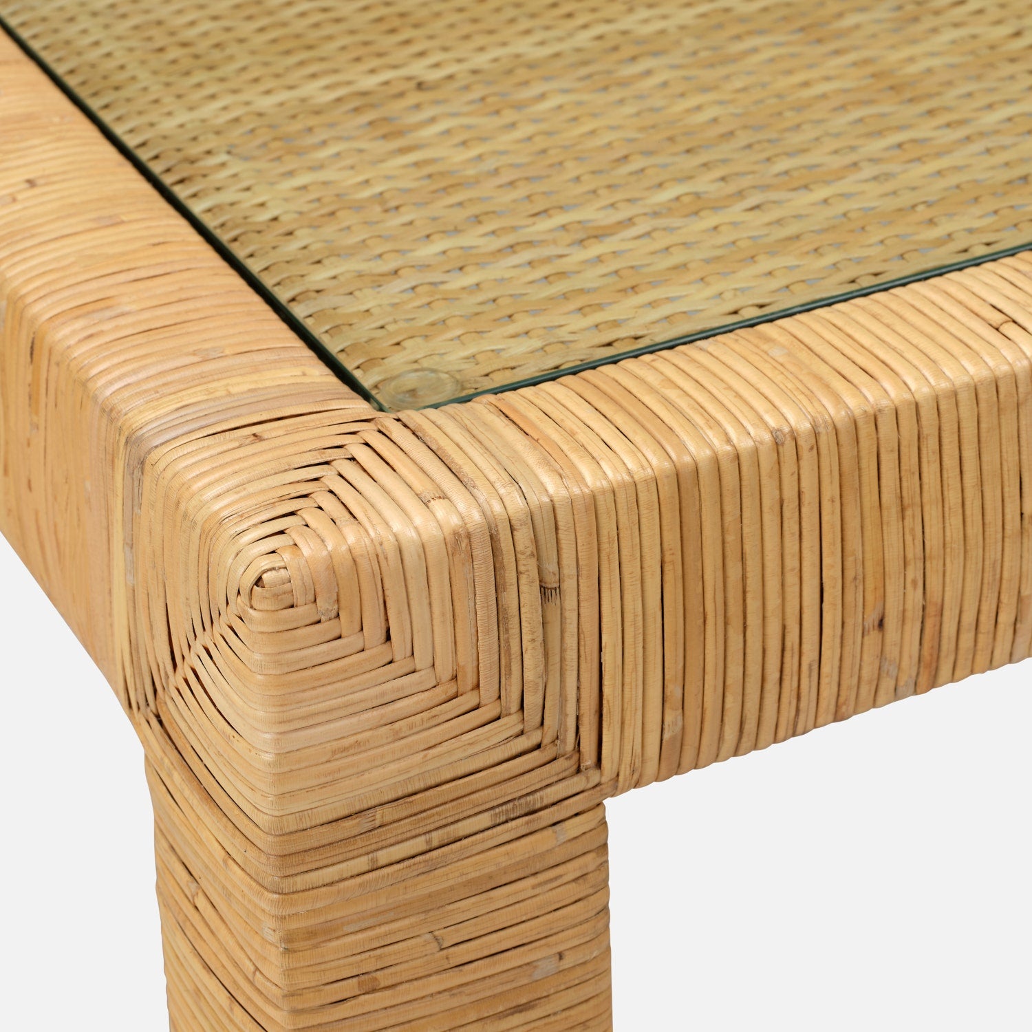 Close-up of the Isla Game Table by Made Goods, showing a corner of its natural rattan base with glass top and highlighting the detailed texture and expert craftsmanship.