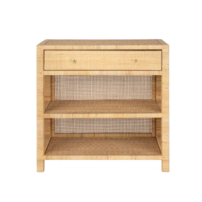 The Isla Nightstand Collection by Made Goods features a rectangular rattan nightstand with a soft-close drawer, two open shelves, and woven back panel, shown against a white background.