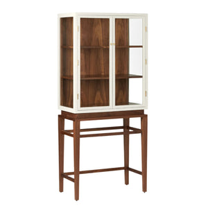 The Made Goods Jamison Cabinet has a white-framed top with glass doors and shelves, set over a brown wooden base with refined walnut legs.