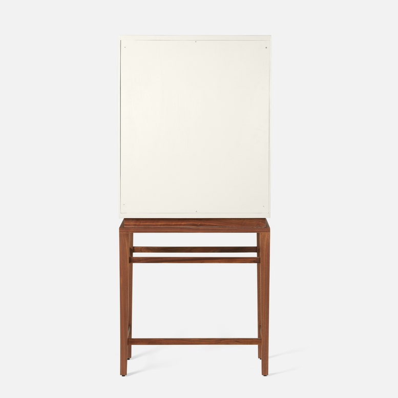 The Jamison Cabinet by Made Goods, a white rectangular panel with a simple modern design, stands vertically on walnut legs atop a wooden table against a plain background.
